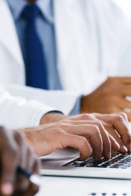 Closeup shot of a group of doctors using a laptop during a meeting in a hospital boardroom